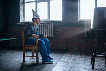 Afraided man in aluminum foil helmet sits in chair