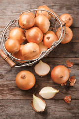 Basket with fresh raw yellow onion on wooden background