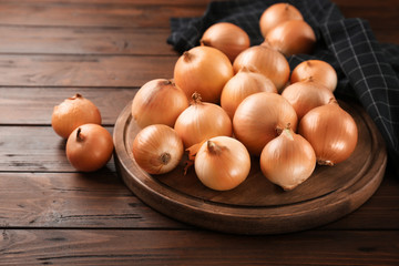 Board with fresh raw yellow onion on wooden background