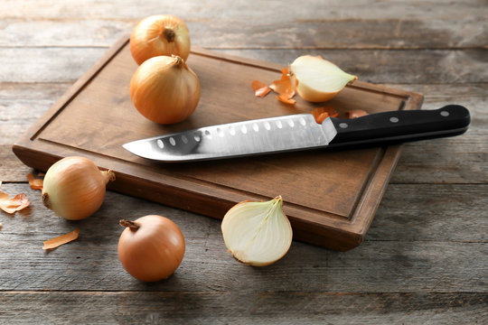 Board with fresh raw yellow onion and knife on wooden background