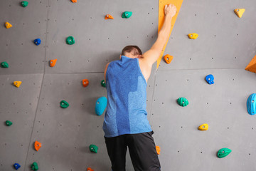 Fototapeta premium Young man climbing wall in gym