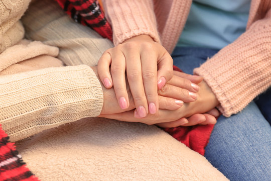 Senior woman and young caregiver holding hands, closeup