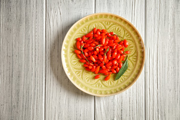 Plate with fresh goji berries on wooden table