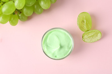 Jar of body cream with grape on color background