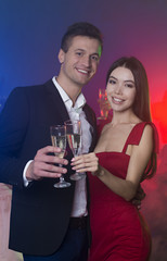 A group of young cheerful and happy friends are dancing at a party. A man and a woman are dancing in the foreground and clinking glasses with champagne