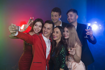 Photo from the party. Friends rest and dance in the club on holiday. The guy with the girl do selfie on the phone
