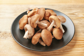 Plate with raw shiitake mushrooms on wooden table