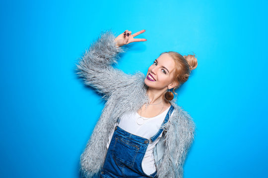 Attractive hipster girl in fluffy coat on color background