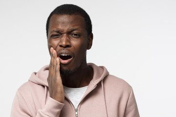 Young black man isolated on gray background wihh mouth open, touching his face with expression of...