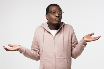 I don't know. Young afrcian man isolated on grey background being at a loss, showing helpless...