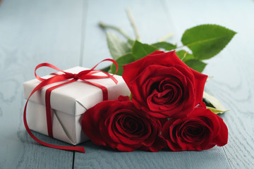 three red roses on blue wood table with gift box