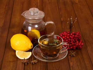 Pitcher of hot tea and lemon, cup and saucer, bunch viburnum berries, on background table