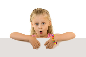 Surprised little girl with long hair standing behind an empty banner, isolated on white