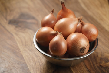 brown onions in steel bowl on old wood table