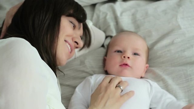 Happy mother with baby lying on bed, top view