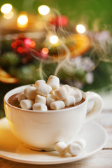 Warm cocoa cup with marshmallows. Christmas lights and decoration blurred in the background.