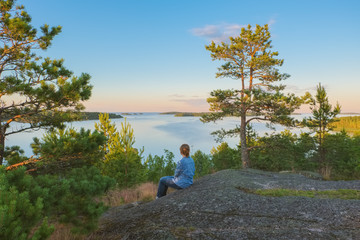 Landscape on the high stone shore of the big Ladoga lake with a sitting girl in the sunny evening
