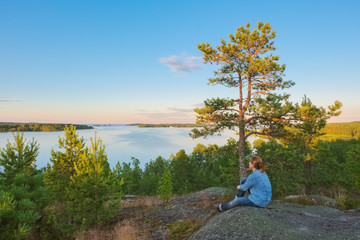 Landscape on the high stone shore of the big Ladoga lake with a sitting girl in the sunny evening