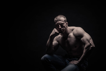 Fototapeta premium portrait of a seated male bodybuilder, on a black background isolated. monochrome. The concept of a photo of competing sports, health, fitness