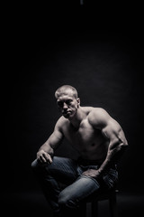 Fototapeta na wymiar portrait of a seated male bodybuilder, on a black background isolated. monochrome. The concept of a photo of competing sports, health, fitness