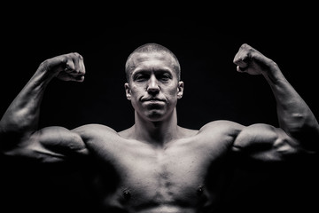 portrait of a male bodybuilder, straining muscles in sports poses, on a black background is...