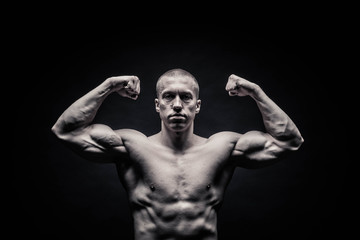 Fototapeta na wymiar portrait of a male bodybuilder, straining muscles in sports poses, on a black background is isolated. monochrome. The concept of a photo of competing sports, health, fitness