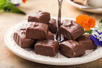 Soft nougat chocolate sweets on white plate with pansy flowers. Party food concept.