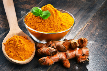 Composition with bowl of turmeric powder on wooden table