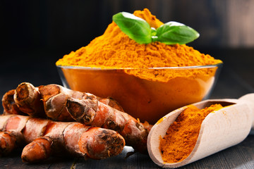 Composition with bowl of turmeric powder on wooden table