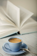 Coffee in a light blue cup and book in blue cover on a wooden background.