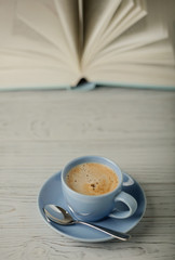 Coffee in a light blue cup and book in blue cover on a wooden background.