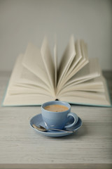 Coffee in a light blue cup and book in blue cover on a wooden background.