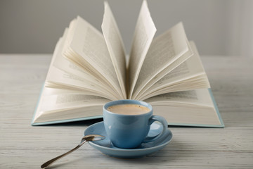 Coffee in a light blue cup and book in blue cover on a wooden background.