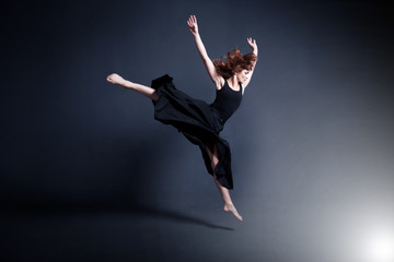 Fototapeta premium Dancer in a black dress is dancing in the dark studio