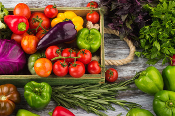 Set of different fresh raw colored vegetables in the wooden tray, light wooden background