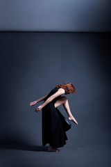 Dancer in a black dress is dancing in the dark studio