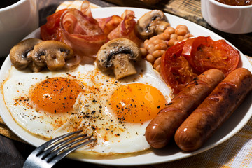 Fried eggs with bacon, sausages and vegetables, closeup