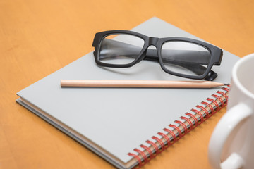Work and education concept. Reading glasses, pencil, notebook and cup of hot coffee on wooden table.