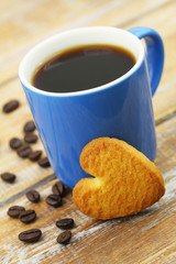 Heart shaped cookie leaning against cup of coffee on rustic wooden surface
