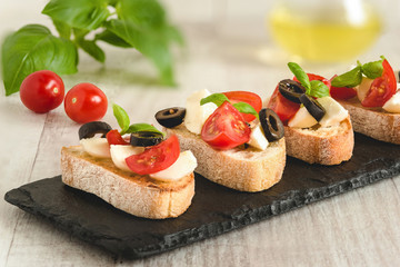 Fototapeta na wymiar Bruschetta italian snack sandwiches with mozzarella, tomatoes and black olives decorated by basil leaves.