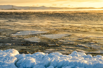 Fototapeta na wymiar Ice floes floating on the fog water in the lake Baikal. Sunset