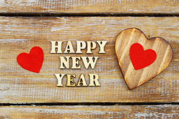 Happy New Year written with wooden letters with hearts on rustic surface
