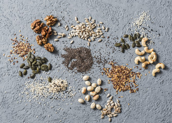 Superfood ingredients. Assortiment seeds and nuts on a gray background, top view. Flax seeds, sesame seeds, walnuts, sunflower seeds, cashews, pumpkin seeds, peanuts. Healthy food concept