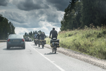 Naklejka premium group of tourists with backpack travels with bicycle outdoors on the asphalt road