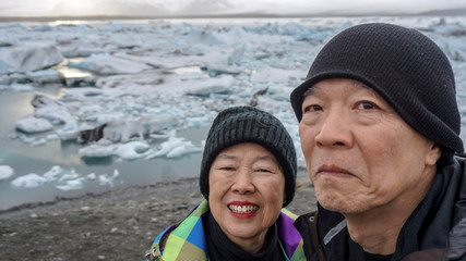 Fototapeta na wymiar Asian senior couple fun trip in Iceland, majestic glacier lagoon landscape