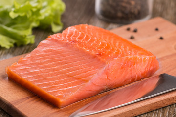 A piece of smoked salmon. On a wooden cutting board with a knife.