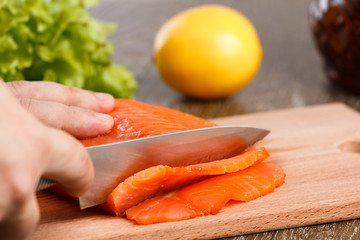 A piece of smoked salmon. On a wooden cutting board with a knife.