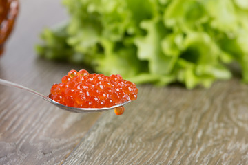 Spoon with red caviar on a background of salad.