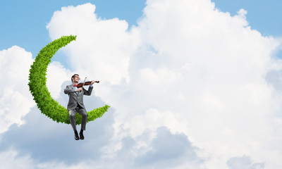 Handsome violinist on moon in blue sky play his melody