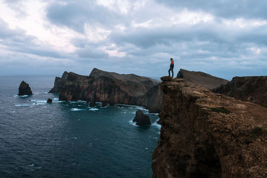 Adult male standing over the rocky ocean cliffs of Madeira, Portugal with dramatic sky during evening blue hour